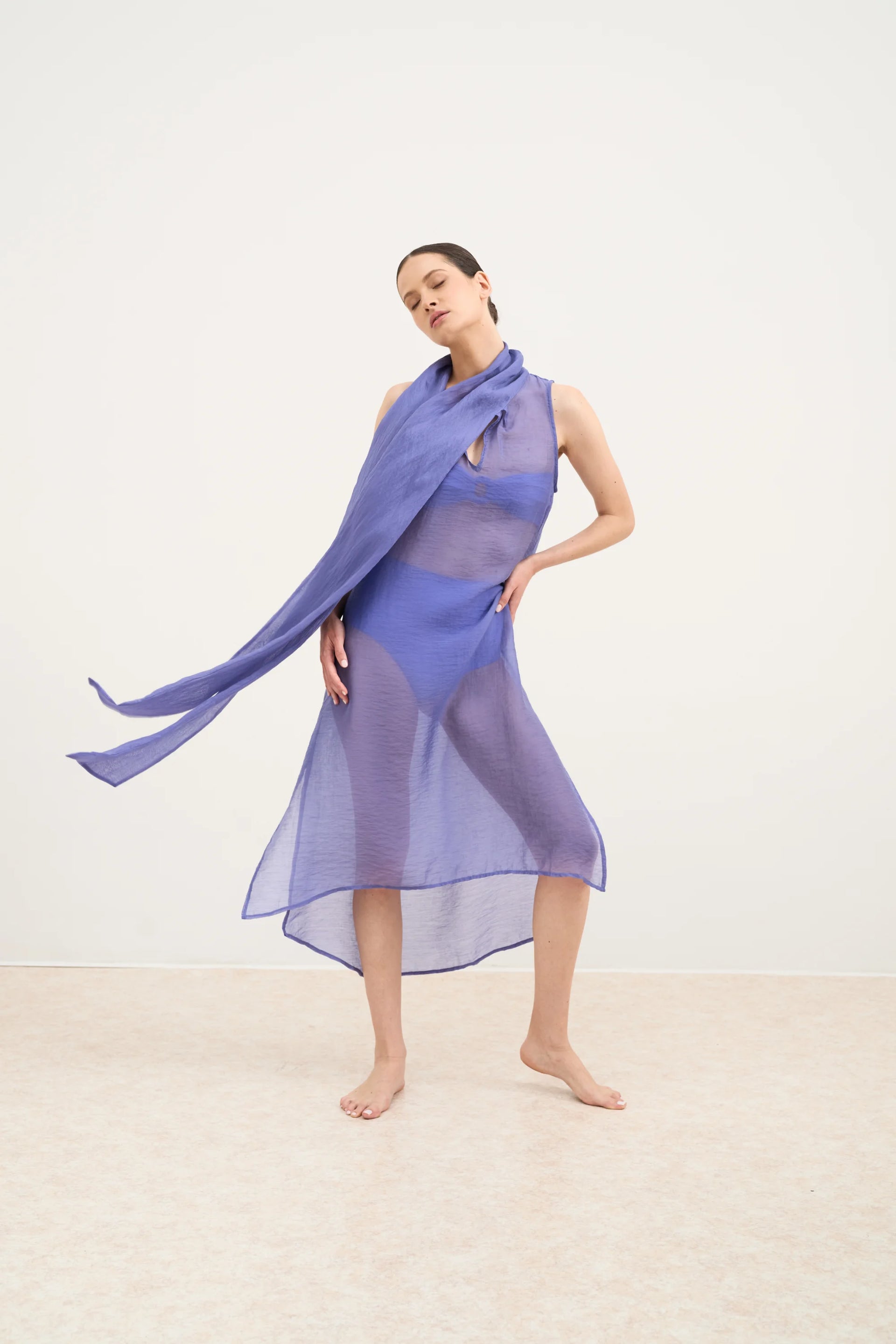 Woman wearing a sheer purple dress with a matching scarf on a white background
